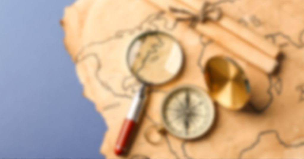 A blurred photo of a map, magnifying glass, and compass.