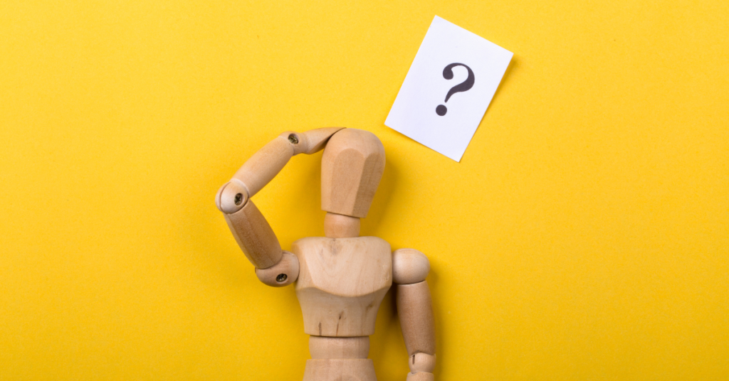 Wooden figurine posed scratching its head, with a question mark above the head