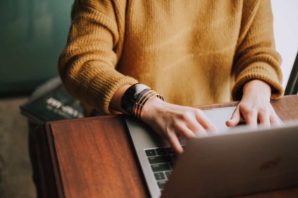 A seated person wearing a mustard yellow sweater works on a laptop.