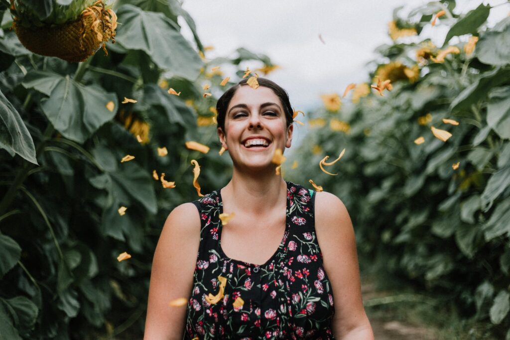 A woman wearing a floral print top smiles in a field of sunflowers