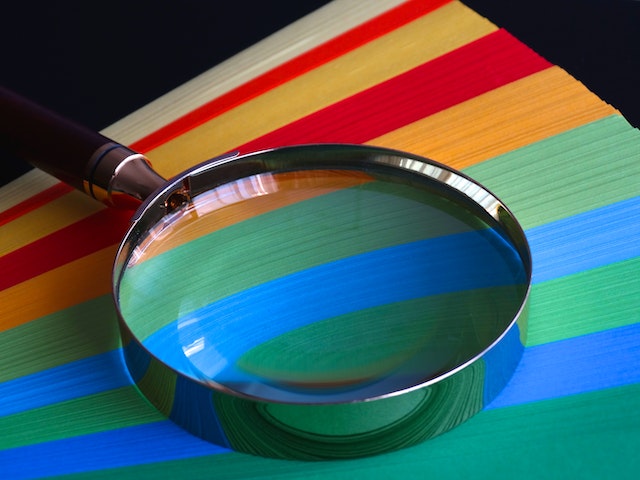 A magnifying glass rests atop a stack of colorful paper.