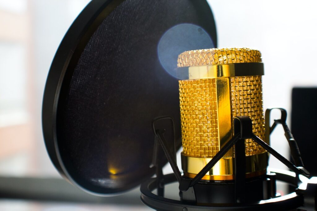 A golden microphone behind a pop filter.